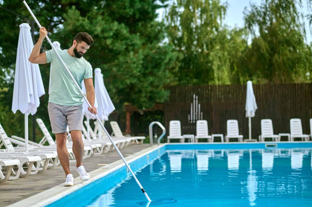 a-service-person-cleaning-the-swimming-pool-and-looking-busyjpg - Wrigley's Pool Co. - Wrigley's Pool Co. Wrigley's Pool Co technician performing weekly pool service on a backyard pool